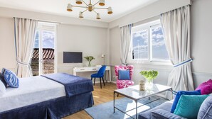 Ein modernes Hotelzimmer mit Bett, Schreibtisch, Sessel, Sofa und Fernseher.