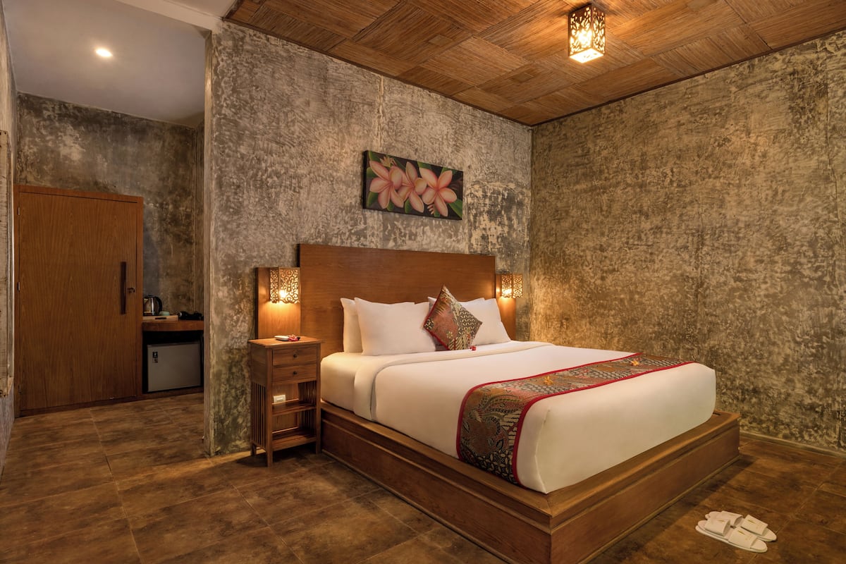 A bedroom with a wooden headboard, a bed with white bedding, a nightstand with a lamp, and a painting on the wall.