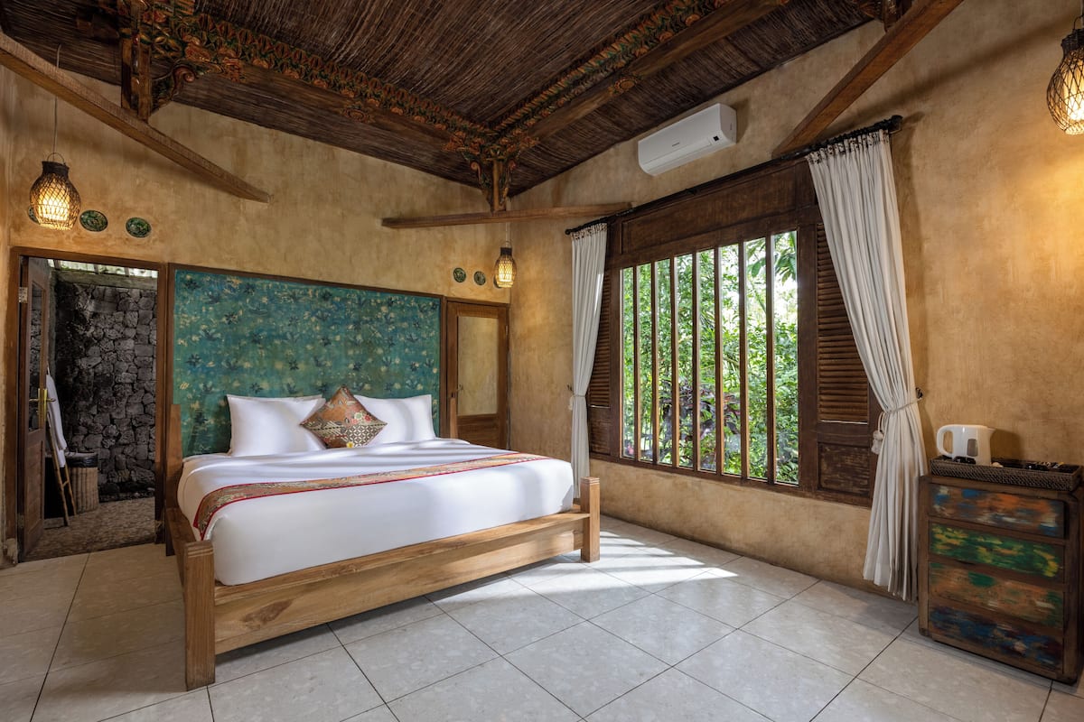 A bedroom with a large bed, wooden beams, a stone wall, and a window with curtains.