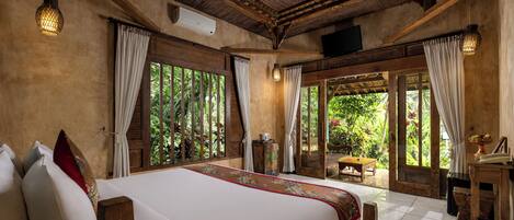 A spacious bedroom with a large bed, wooden ceiling, and a view of lush greenery outside.