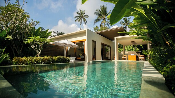 A clear swimming pool with a modern house in the background, surrounded by lush greenery and palm trees. - Senetan Villas and Spa Resort (Payangan)