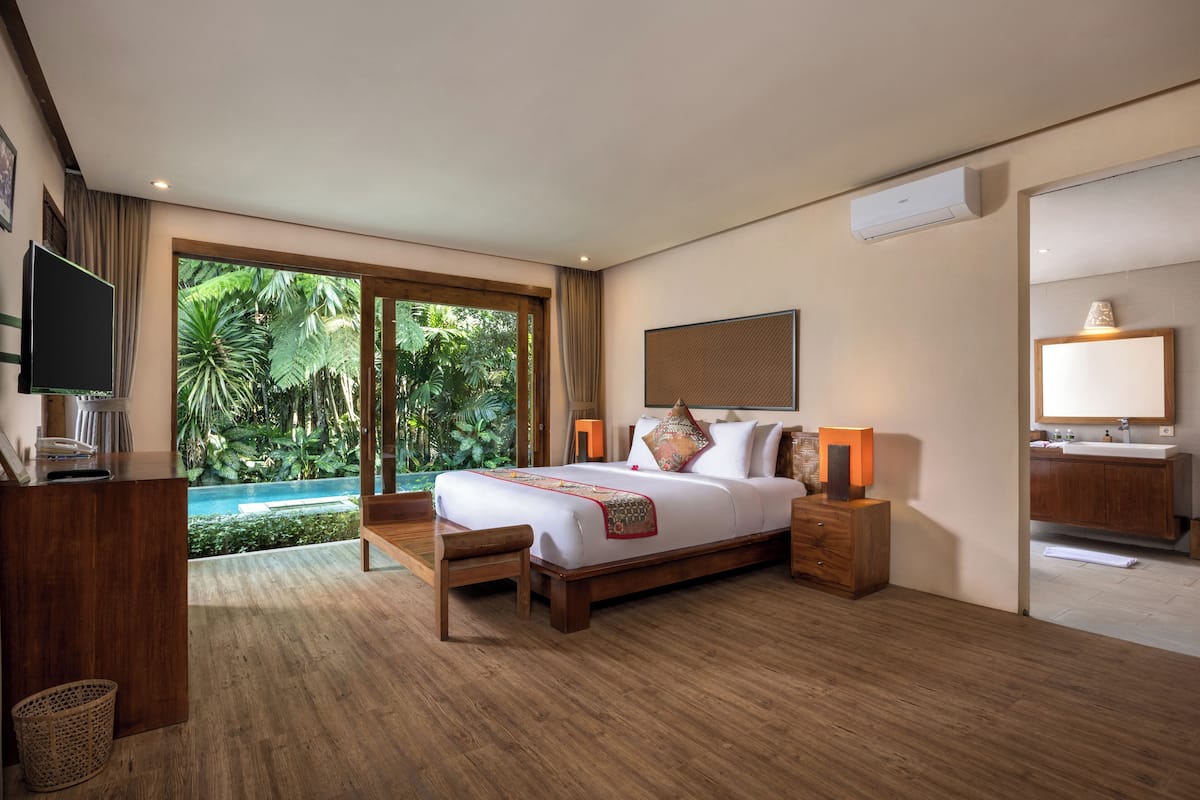 A spacious bedroom with a large bed, wooden furniture, a TV, and a view of a swimming pool.