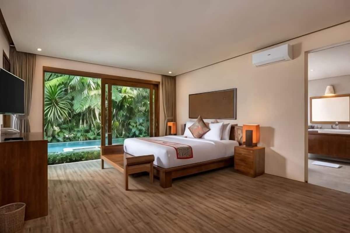 A bedroom with a bed, bedside tables, a TV, and a view of a pool.