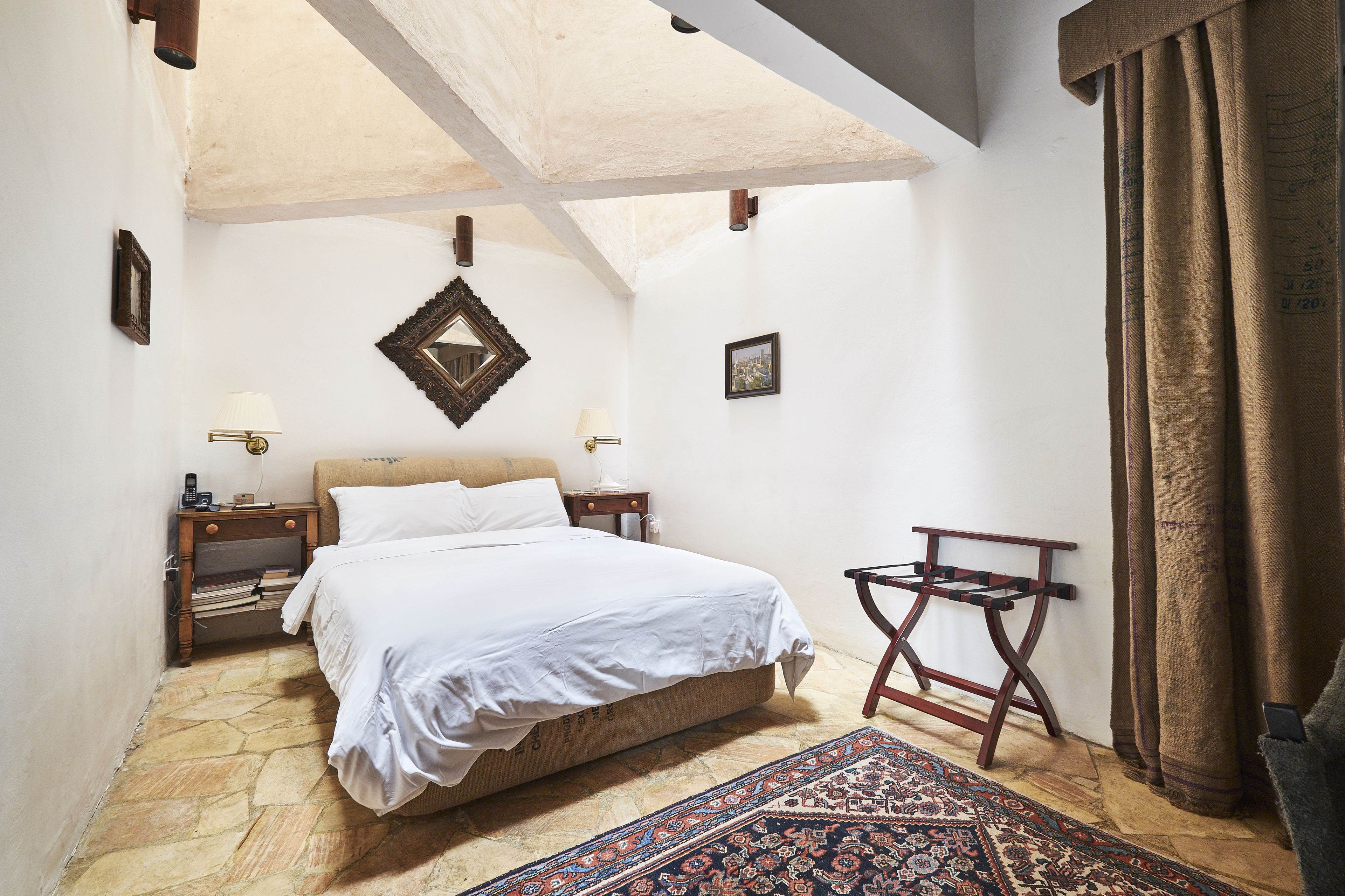 A bedroom with a bed, nightstands, a patterned rug, and a wooden chair.