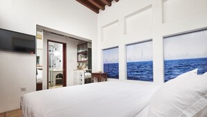 Quarto de hotel com cama, escrivaninha e vista para o oceano através de grandes janelas.