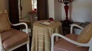 Quarto com duas cadeiras brancas, uma mesinha, um espelho e um candelabro vermelho.
