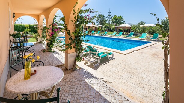 A poolside area with a clear view of the pool, lounge chairs, and a table with a vase of flowers. - Monte dos Avós Apartamentos, Albufeira (Albufeira)