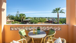 A balcony with wicker chairs and a table, overlooking a landscaped area with palm trees and a view of the sea. - Monte dos Avós Apartamentos, Albufeira (Albufeira)