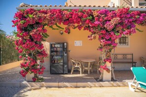 A covered outdoor seating area with a vending machine, a table, and chairs. - Monte dos Avós Apartamentos, Albufeira (Albufeira)