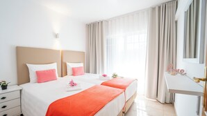 A hotel room with two beds, a nightstand, a vanity with a mirror, and a window with curtains. - Monte dos Avós Apartamentos, Albufeira (Albufeira)