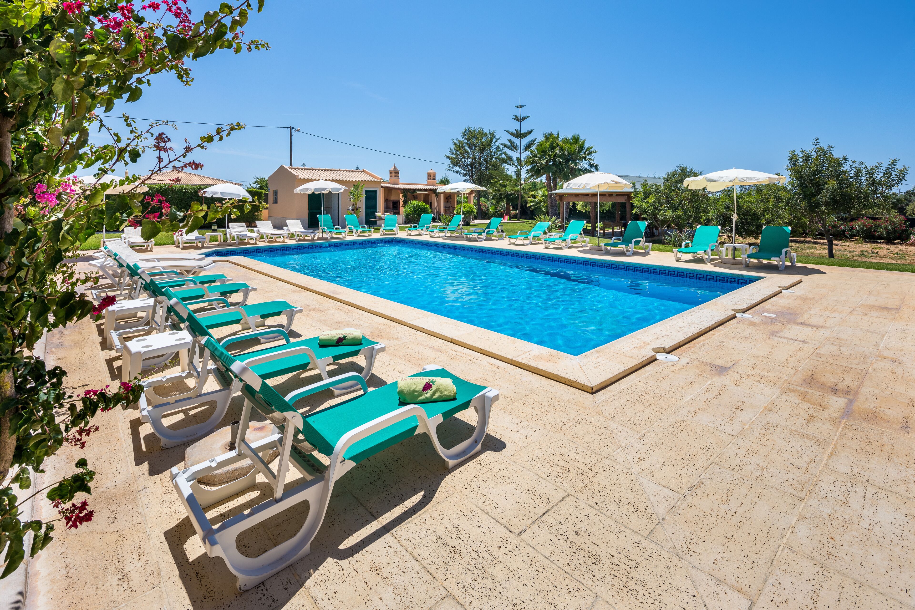 A swimming pool with lounge chairs and umbrellas, surrounded by a landscaped garden and a building in the background.