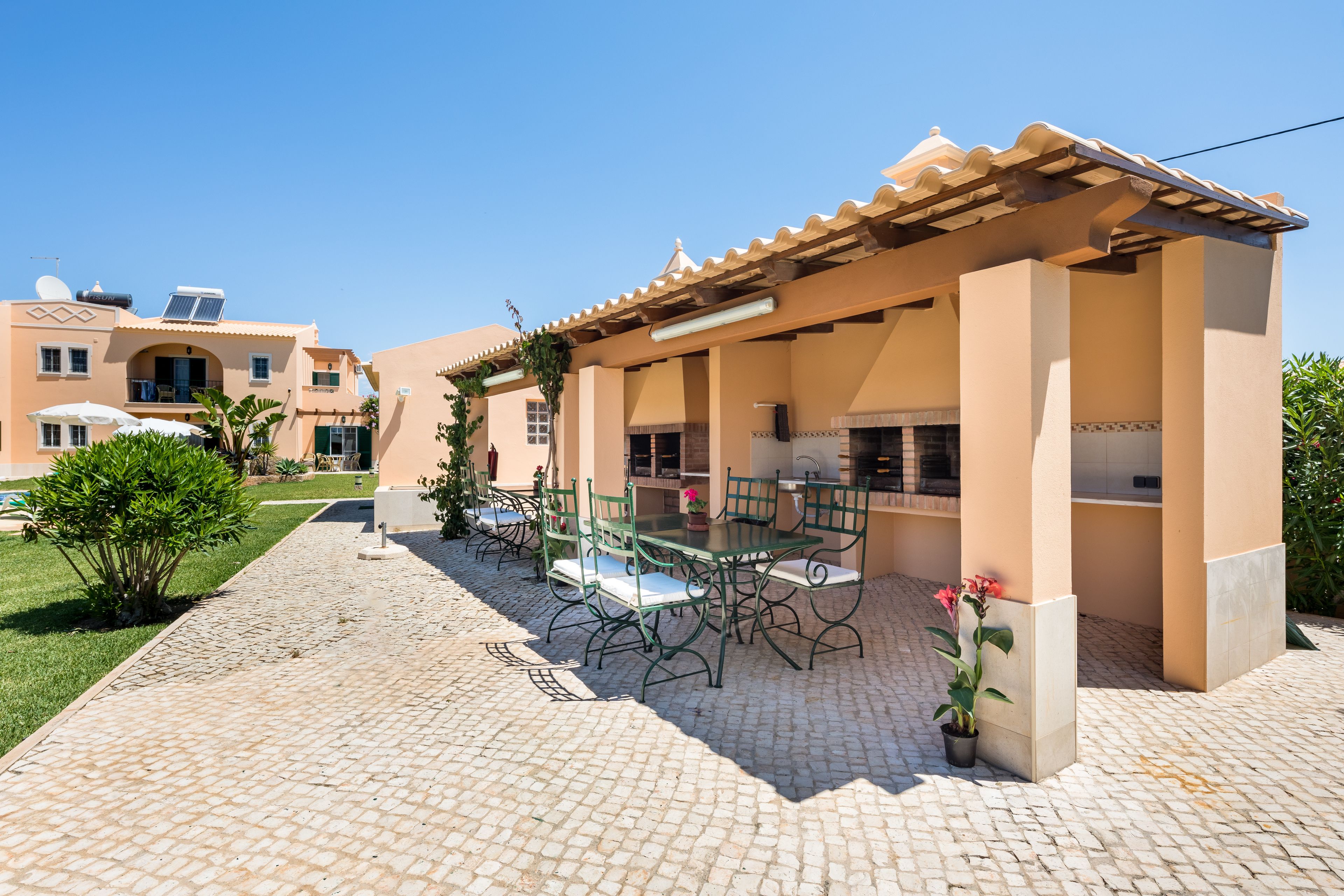 A patio area with outdoor seating and a pergola, surrounded by a cobblestone walkway and greenery.