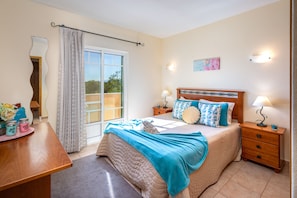A bedroom with a bed, bedside tables, a desk, a chair, a window with curtains, and a view of the outdoors. - Monte dos Avós Apartamentos, Albufeira (Albufeira)