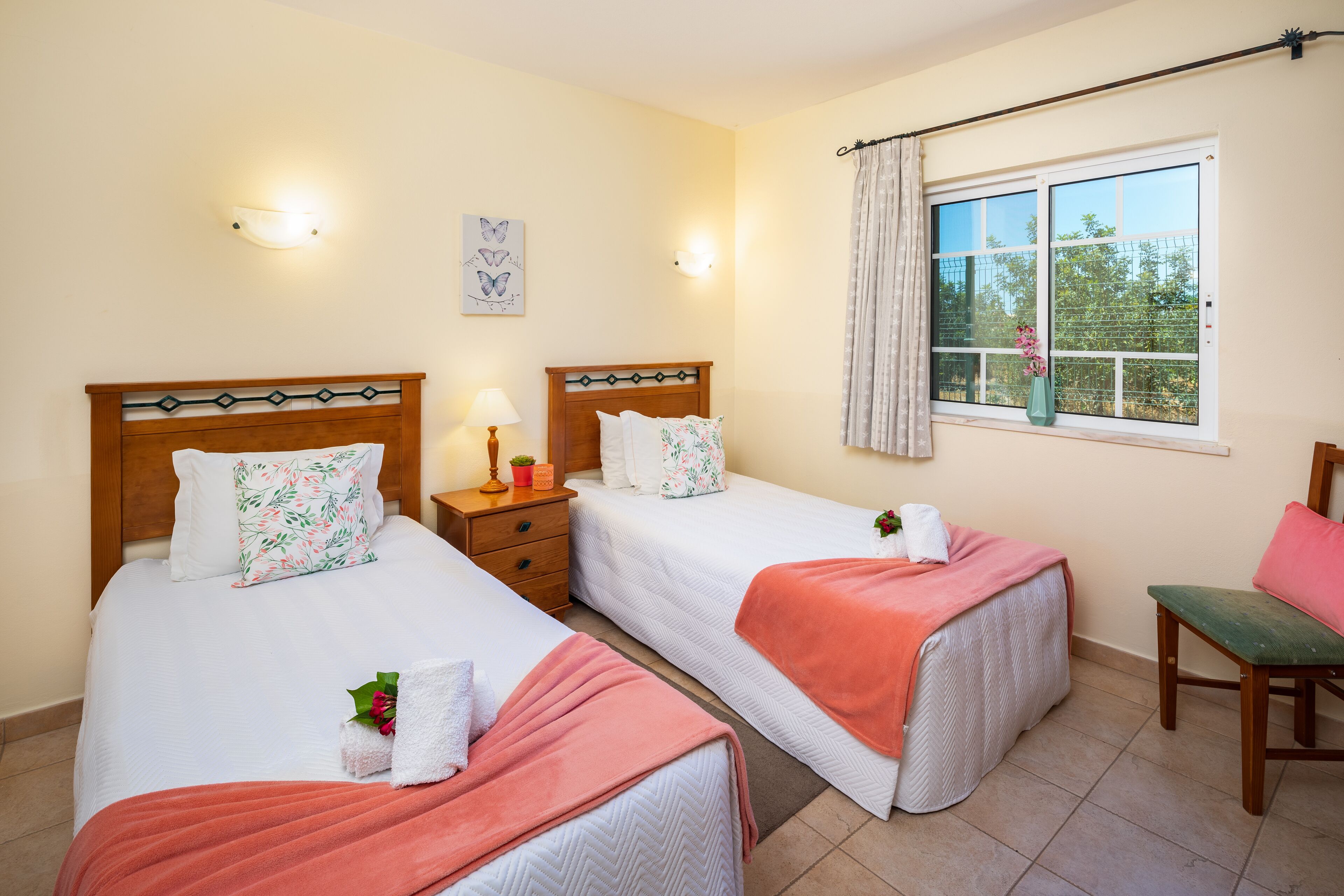 Une chambre d’hôtel avec deux lits, une fenêtre avec des rideaux, une table de chevet avec une lampe et une chaise.