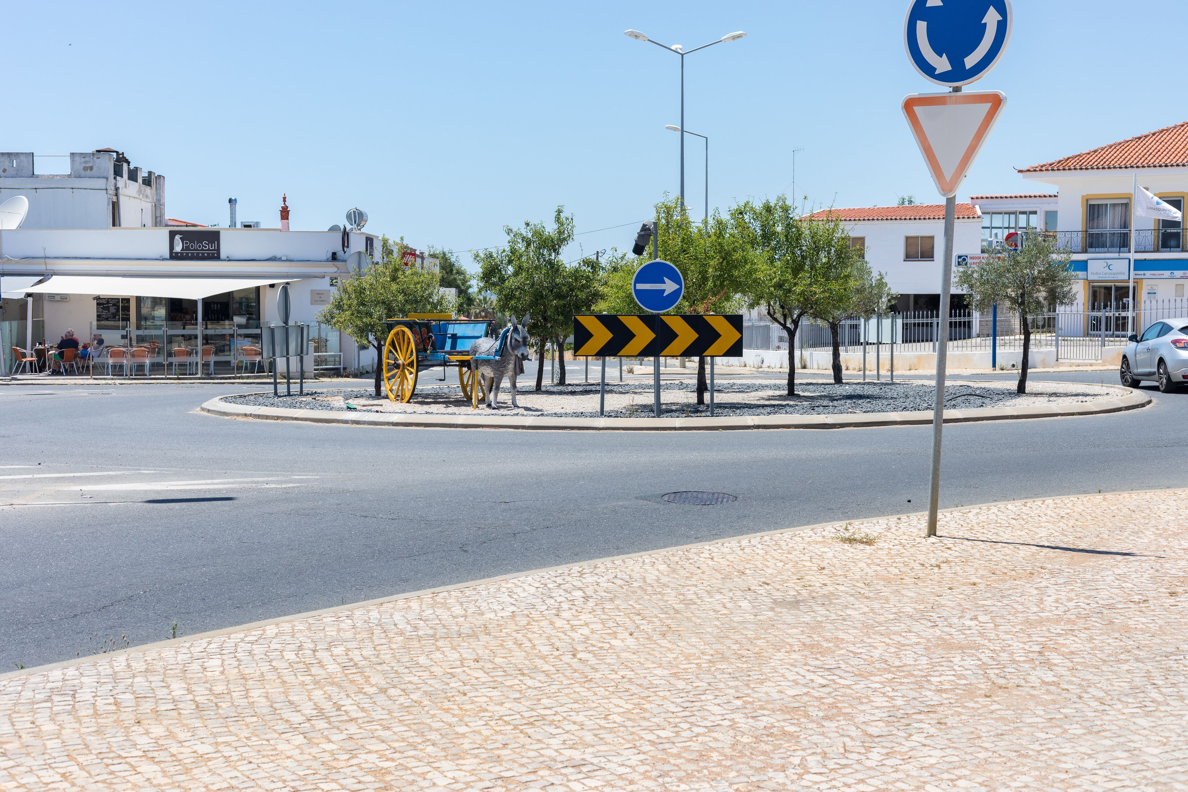 A roundabout with a donkey cart, a blue directional sign, and a triangular yield sign.