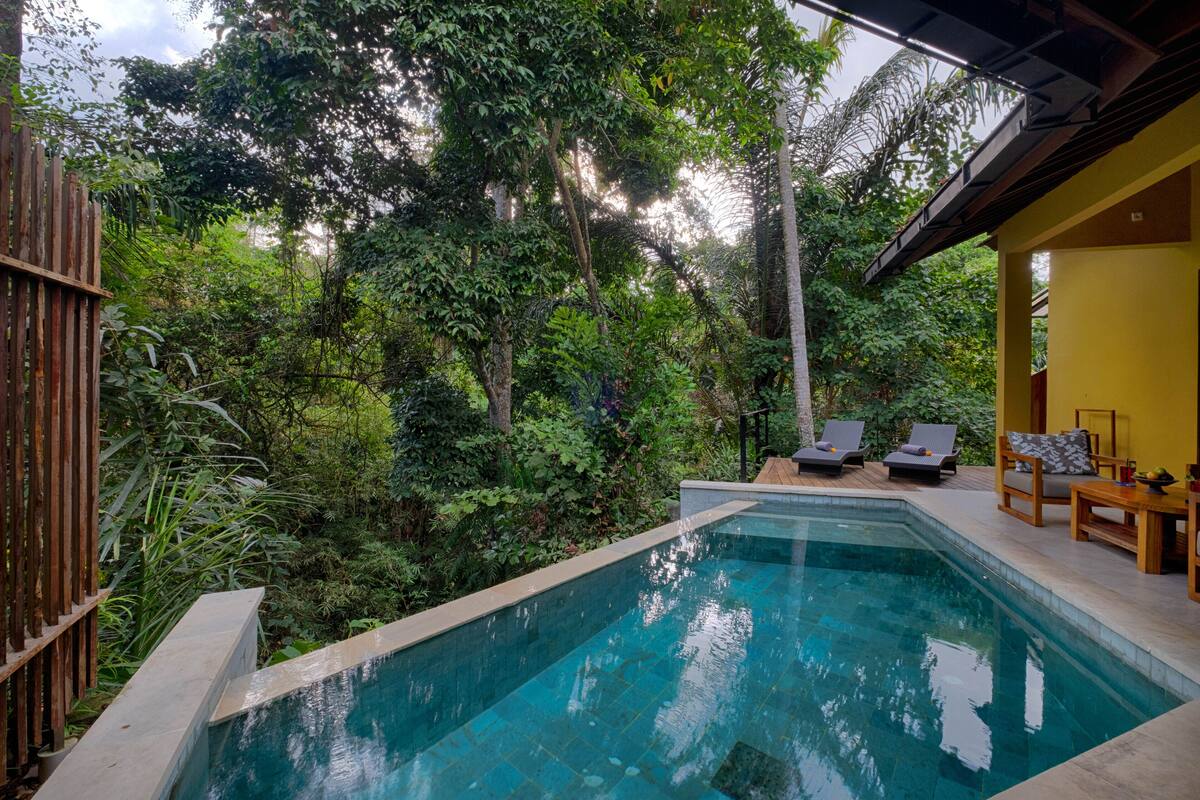 Un área de piscina con cubierta de madera, sillones de descanso y una pared amarilla.