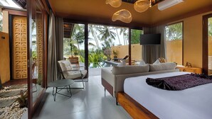 A modern hotel room with a large bed, a sofa, a dining area with a table and chairs, and a view of palm trees. - Samkhya Villas (Ubud)
