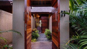 A wooden pathway leading to a building entrance with a tiled roof and a small garden area with plants and rocks. - Samkhya Villas (Ubud)