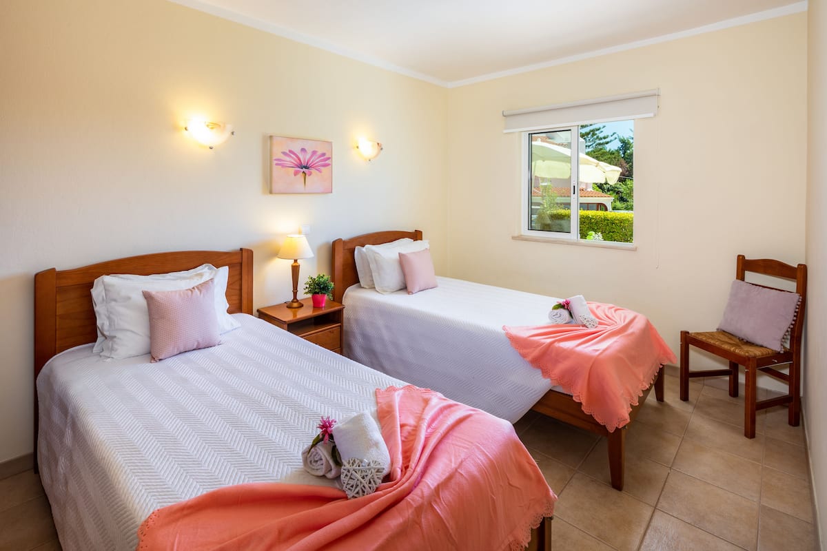 A hotel room with two beds, a window with a view of the garden, and a chair.