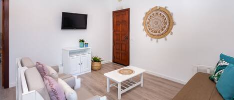 A modern living room with a sofa, a white coffee table, a television, and a decorative wall hanging.