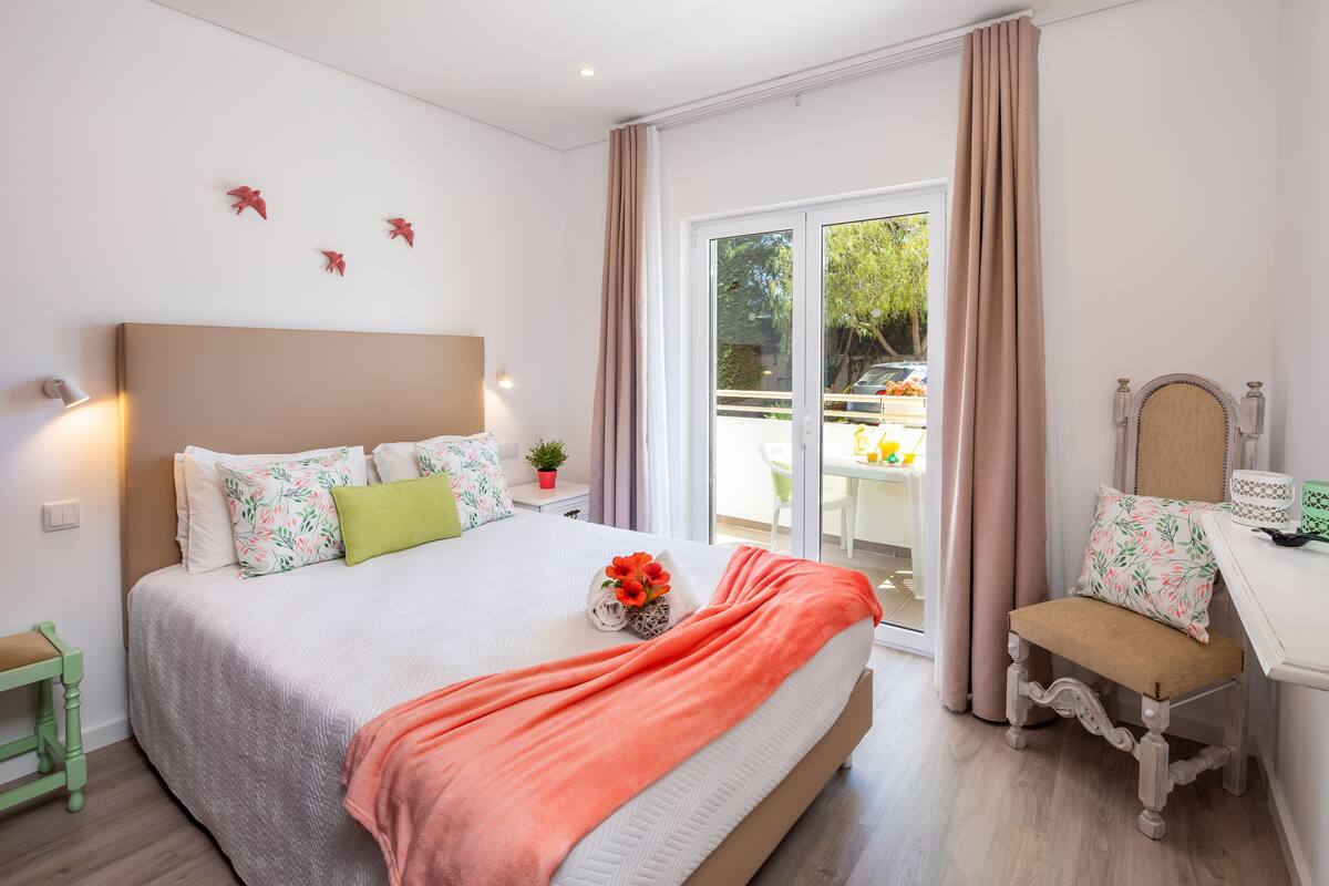 A bedroom with a bed, a chair, a table, and a view of the outside.