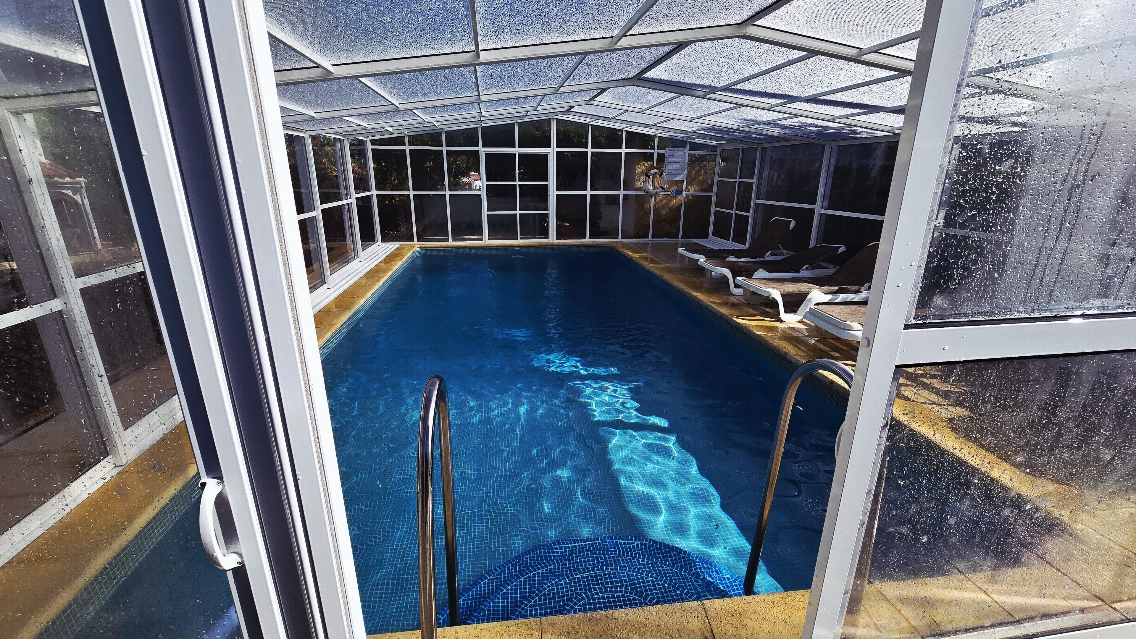 Ein Innenpool mit klarem Wasser, umgeben von Glaswänden und einem Metalldach.