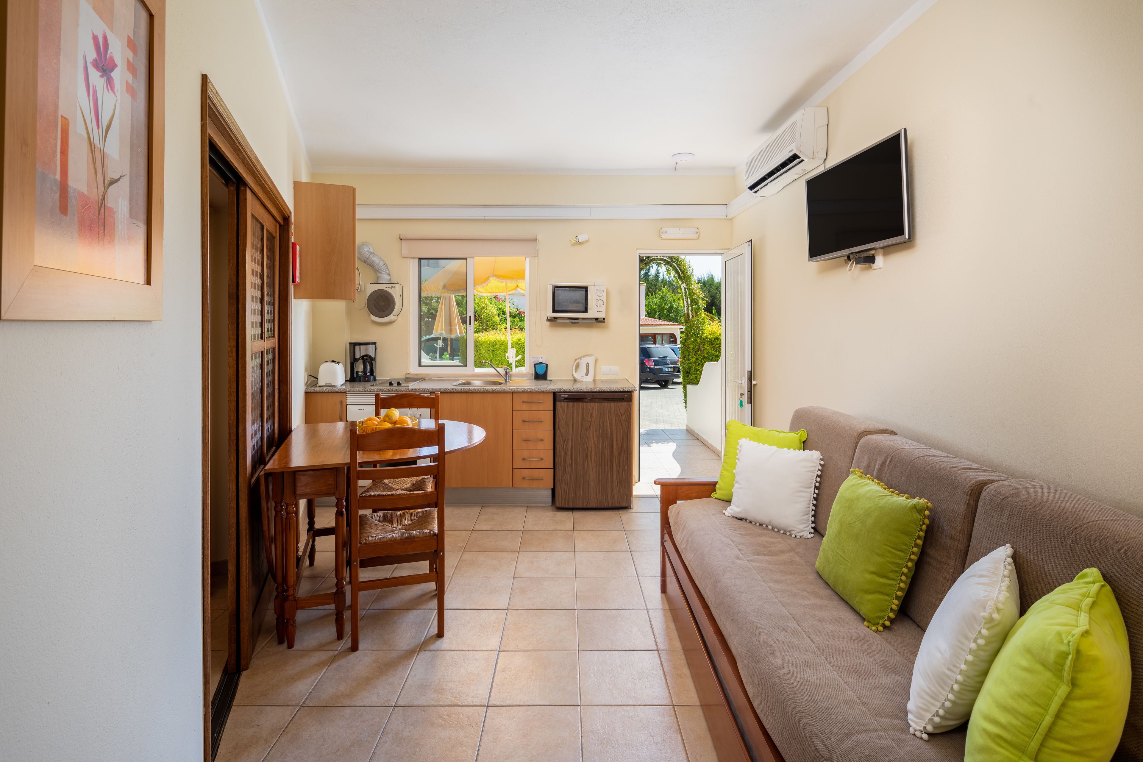 Un espace de vie compact comprenant un coin repas, une kitchenette et un canapé agrémenté de coussins.