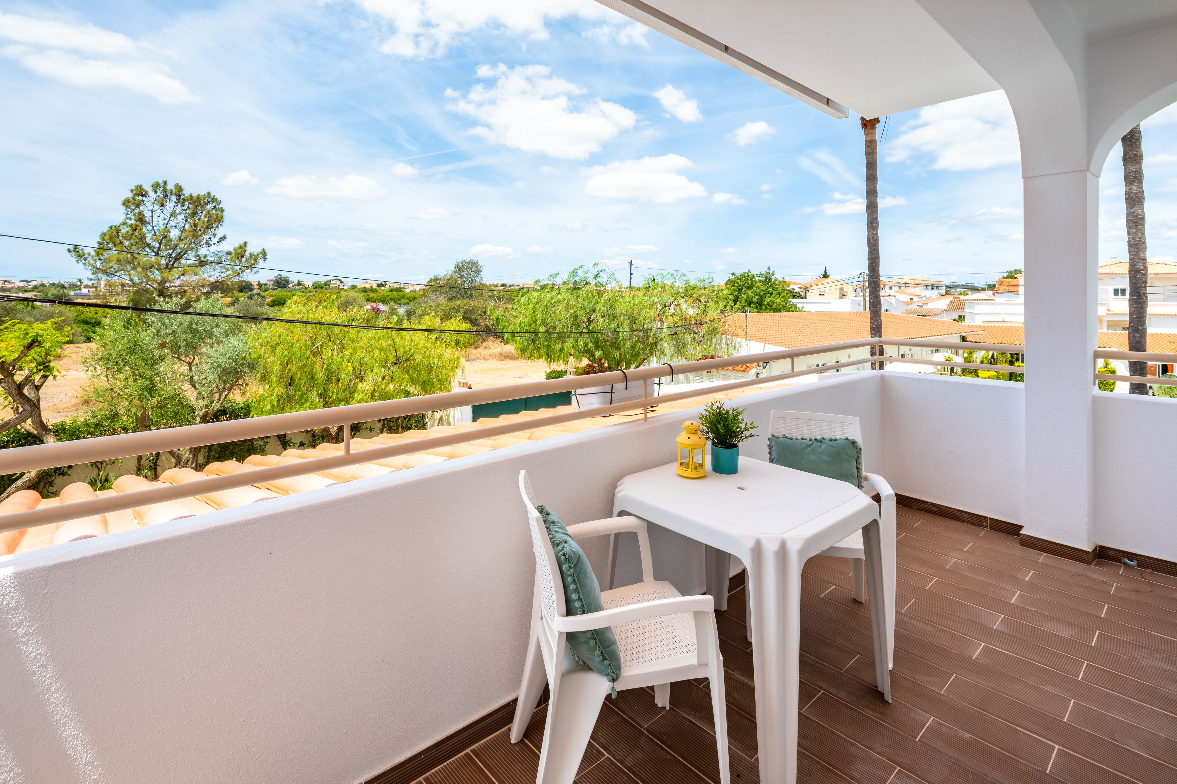 A balcony with a white table and two chairs, a small potted plant, and a yellow lantern.