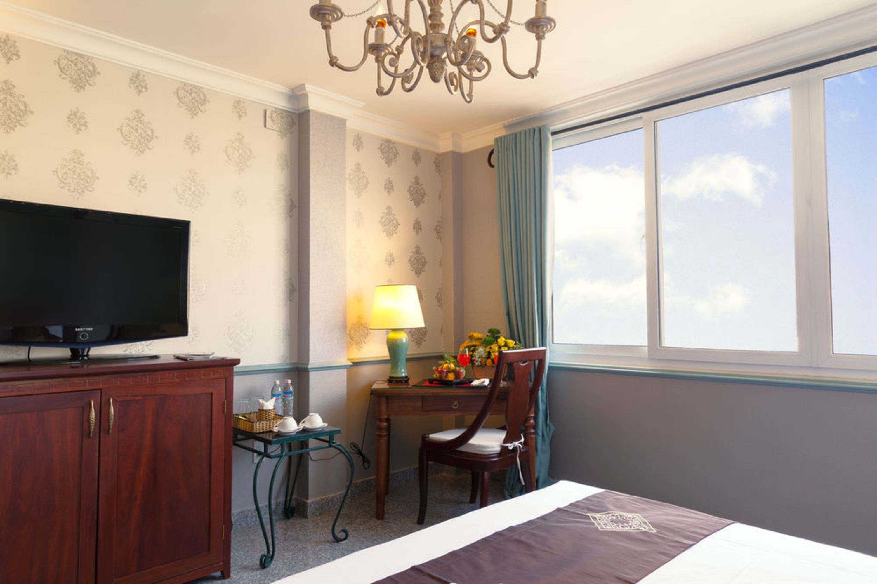 A hotel room with a bed, a television on a wooden cabinet, a desk with a lamp, and a chair.