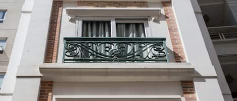 Ein mehrstöckiges Gebäude mit weißer Fassade, Ziegelakzenten und dekorativen Metallgeländern an den Balkonen.