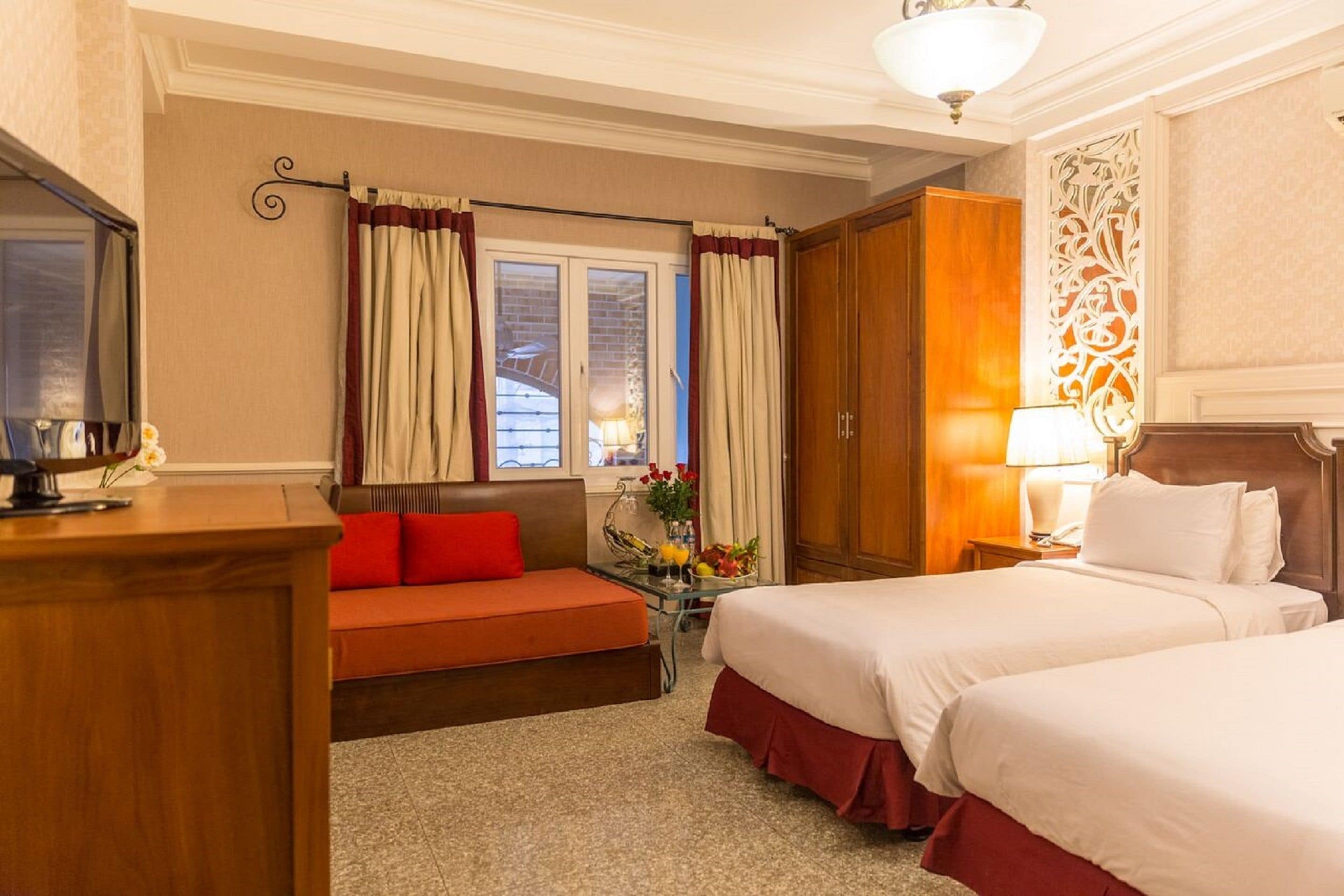 A hotel room with two beds, a desk, a sofa, and a window with curtains.