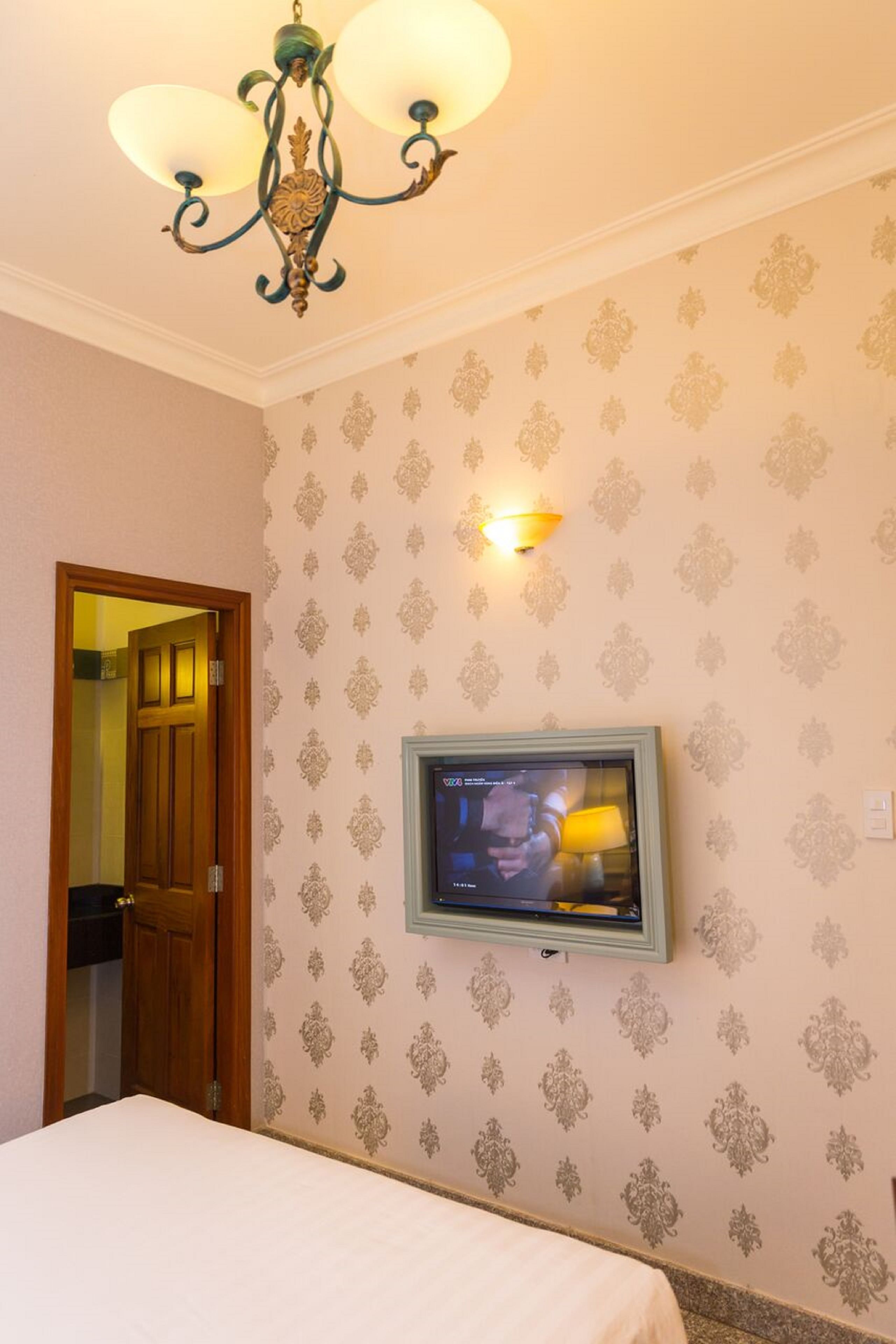 Habitación de hotel con cama, televisor montado en la pared, candelabro y puerta que da a otra habitación.