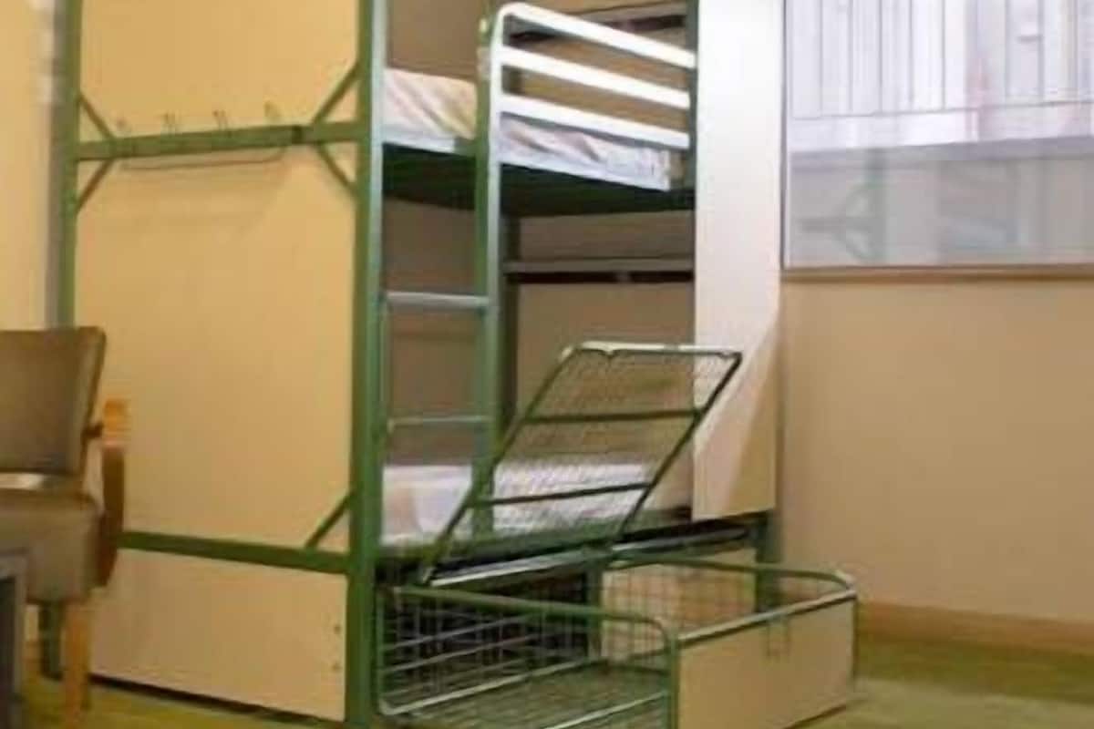 Un lit superposé avec une structure verte, une fenêtre avec des stores et une chaise dans une pièce dont le sol est recouvert d’une moquette.