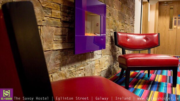 Una habitación con pared de piedra, un espejo morado, una silla roja y una alfombra a rayas colorida.
