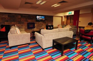 A hotel lobby with sofas, a coffee table, a fireplace, a television, and a bookshelf. - The Savoy Hostel (Galway)