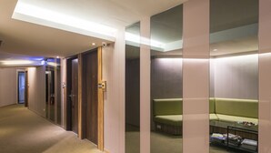 A hotel corridor with a green sofa, a glass table with magazines, and a wooden door. - Shin Shin Hotels - Songshan (Taipei)