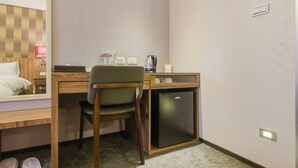 A hotel room with a wooden desk, a chair, a small refrigerator, a mirror, and a bed with a wooden headboard. - Shin Shin Hotels - Songshan (Taipei)