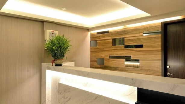 A reception area with a marble counter, a potted plant, a wooden wall with built-in shelves, and a door. - Shin Shin Hotels - Songshan (Taipei)