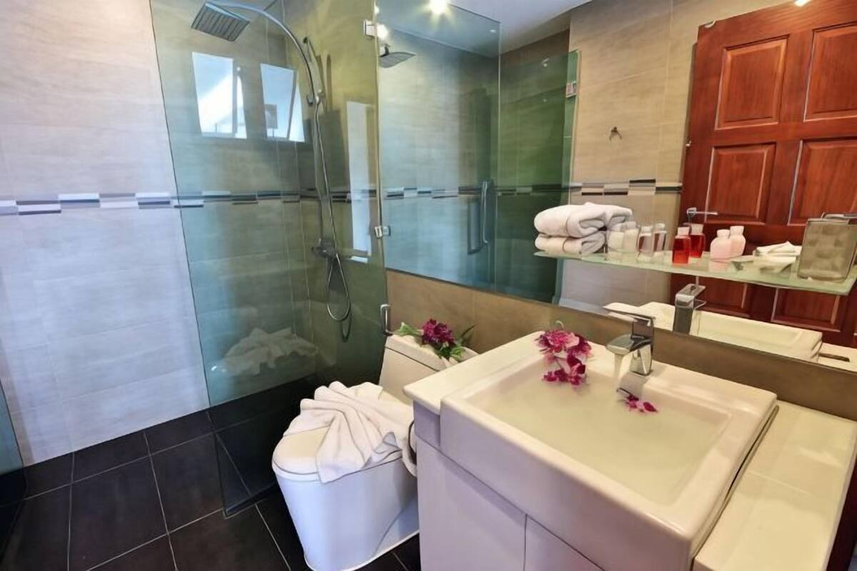 Un bany modern amb un armari de dutxa de vidre, un vàter blanc, un lavabo amb mirall i un moble de fusta amb tovalloles.
