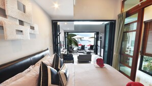 A modern hotel room with a large bed, a view of the outdoor seating area, and a balcony with a view of the sea. - Villa Labaron (Koh Samui)