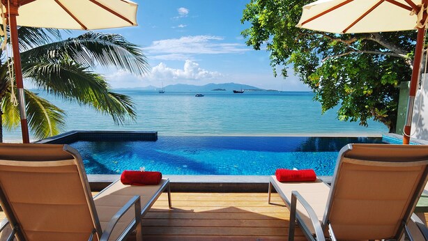 A poolside area with two lounge chairs and umbrellas, overlooking a clear blue sea with boats. - Villa Labaron (Koh Samui)