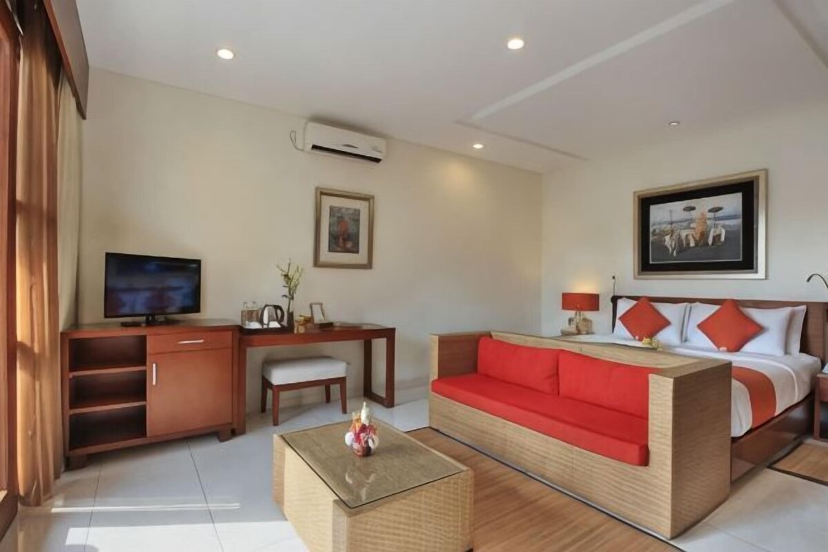 A hotel room with a bed, a sofa, a desk with a television, and a chair.