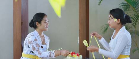 Dos personas sentadas a una mesa con un pastel decorado, rodeadas de flores y un ambiente tradicional.