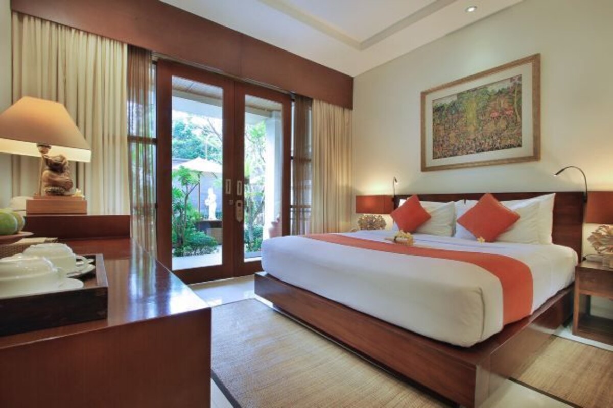 A hotel room with a large bed, a desk with a lamp, and a view of the outdoors through a sliding door.