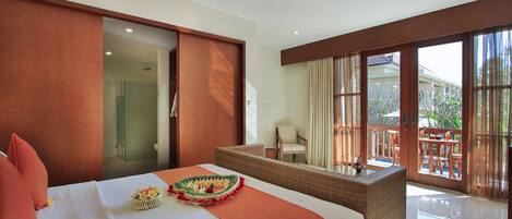 A hotel room with a bed, a small table, a wicker chair, and a balcony with a view.