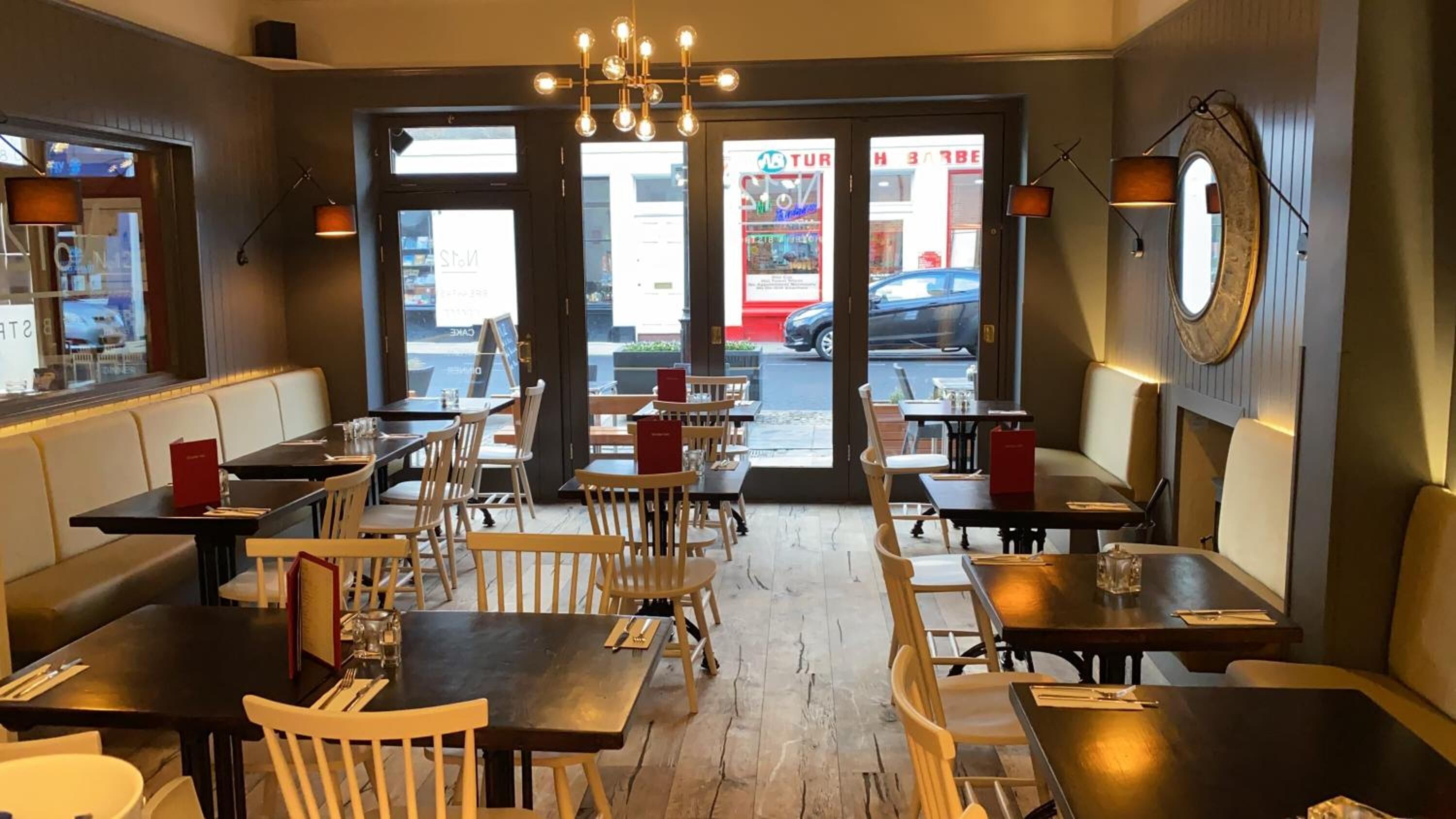 L’intérieur d’un restaurant, avec des tables et des chaises en bois, un lustre et une vue sur la rue.