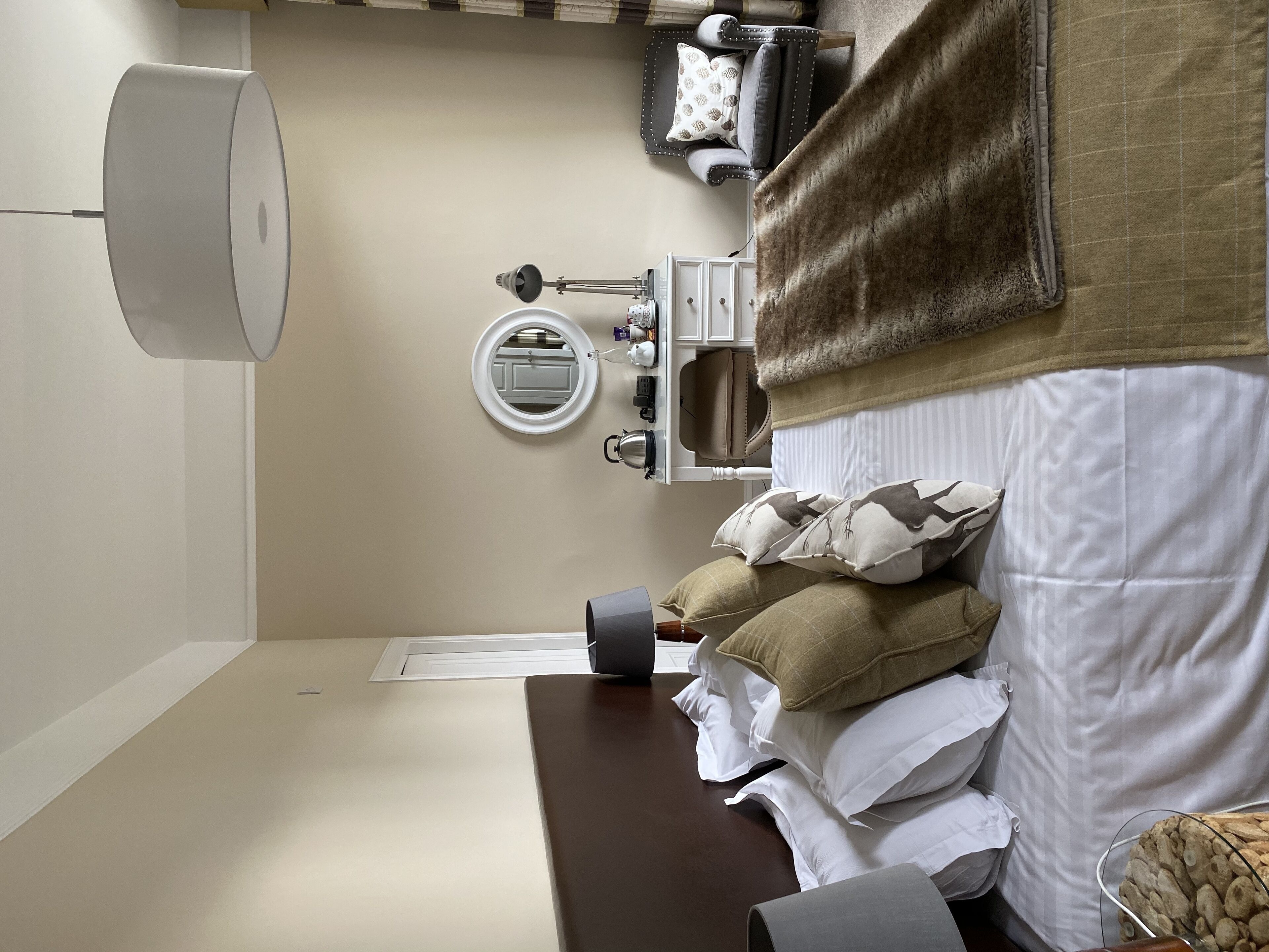 Une chambre à coucher bien rangée, avec un lit, une table de chevet, une lampe et un miroir.