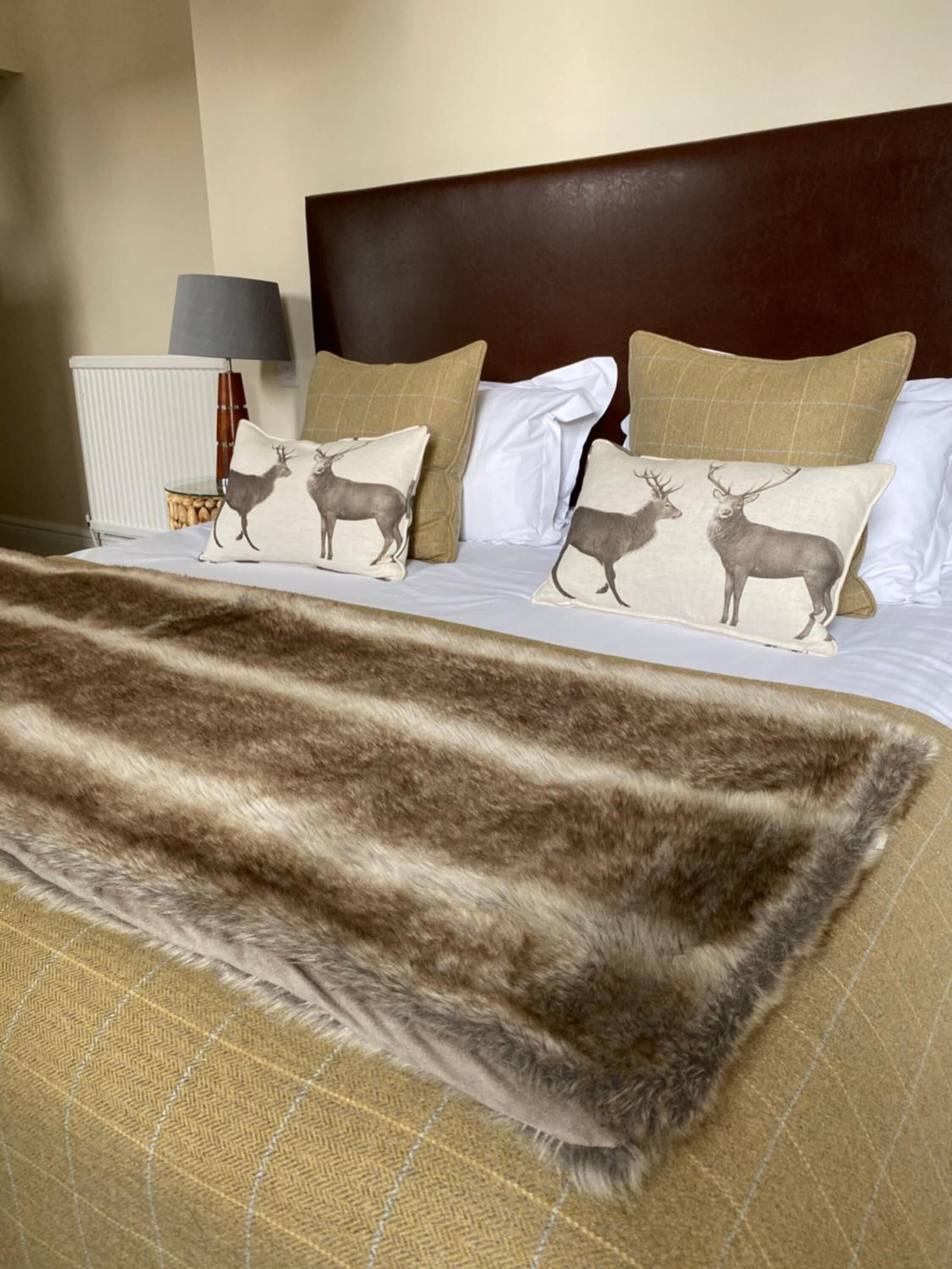 A hotel room with a bed featuring patterned pillows, a fur throw, and a headboard.