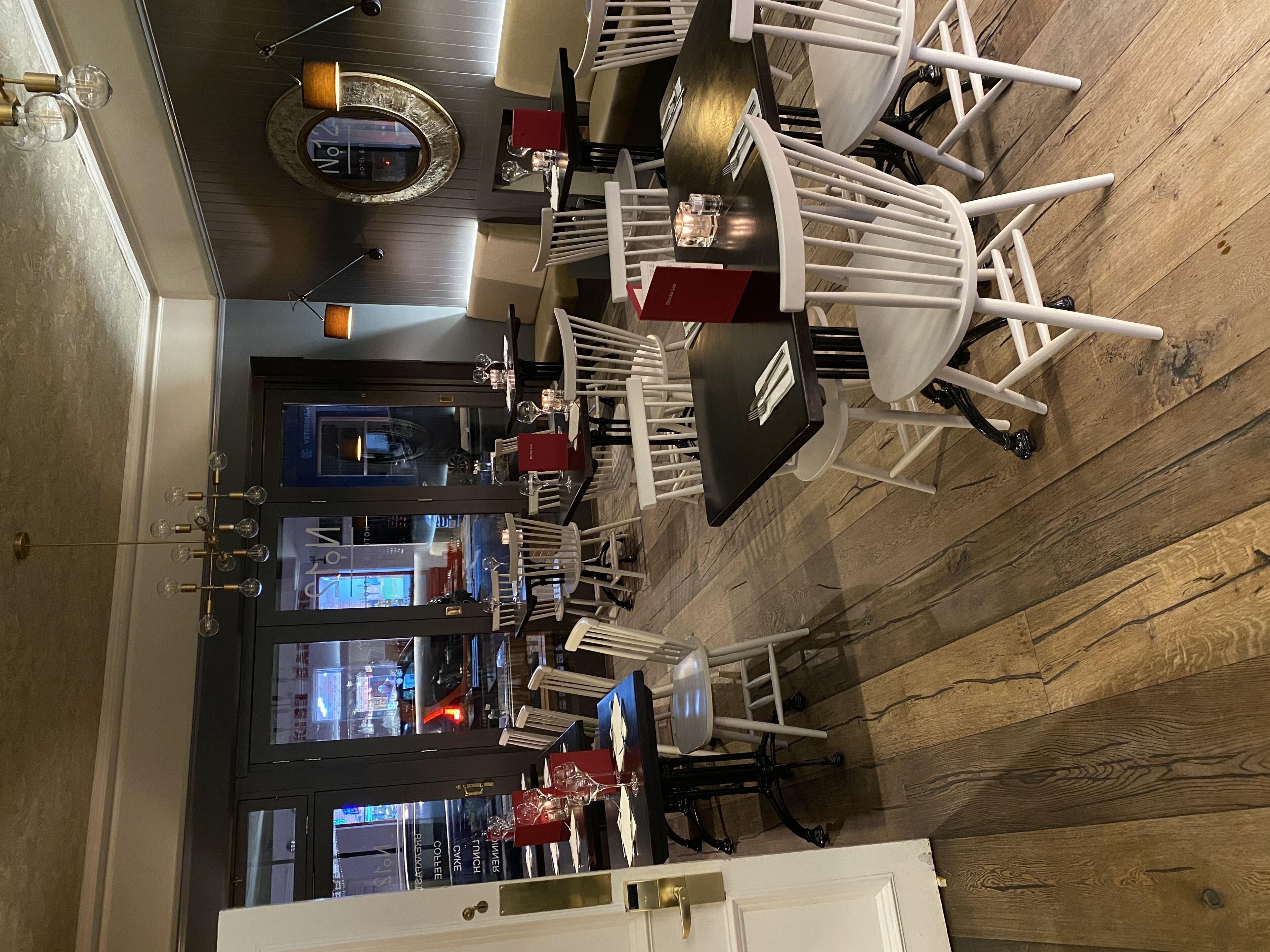 A restaurant with a modern interior, featuring white chairs, a black table, and a wooden floor.