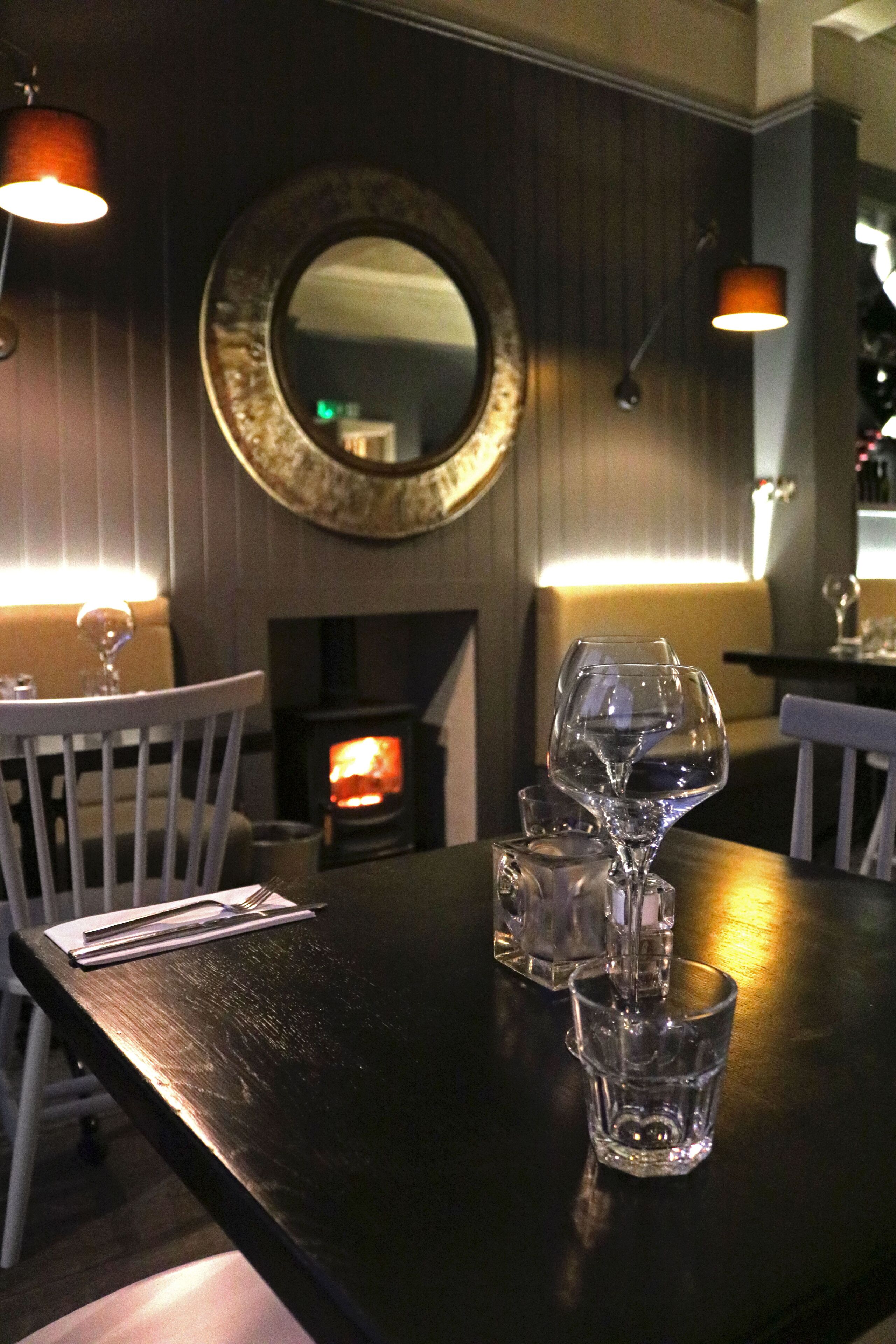 Un interior de restaurante con una mesa de madera, sillas, una chimenea y un espejo en la pared.